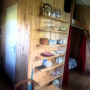 Cabane en bois chaleureuse avec étagères en bois, kitchenette et échelle menant à une chambre.