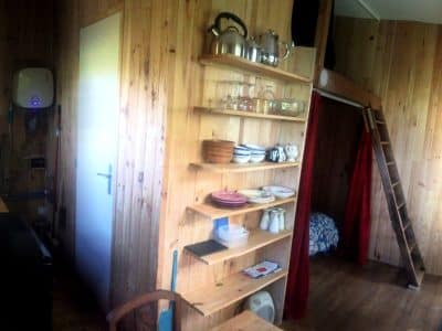 Cabane en bois chaleureuse avec étagères en bois, kitchenette et échelle menant à une chambre.