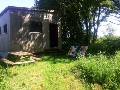 Cabane en bois entourée de verdure, avec une terrasse en bois et des tableaux colorés à l'extérieur.