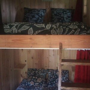 Cabane en bois avec lits superposés, décorée de coussins à motifs floraux. Ambiance chaleureuse.