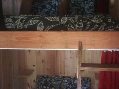 Cabane en bois avec lits superposés, décorée de coussins à motifs floraux. Ambiance chaleureuse.