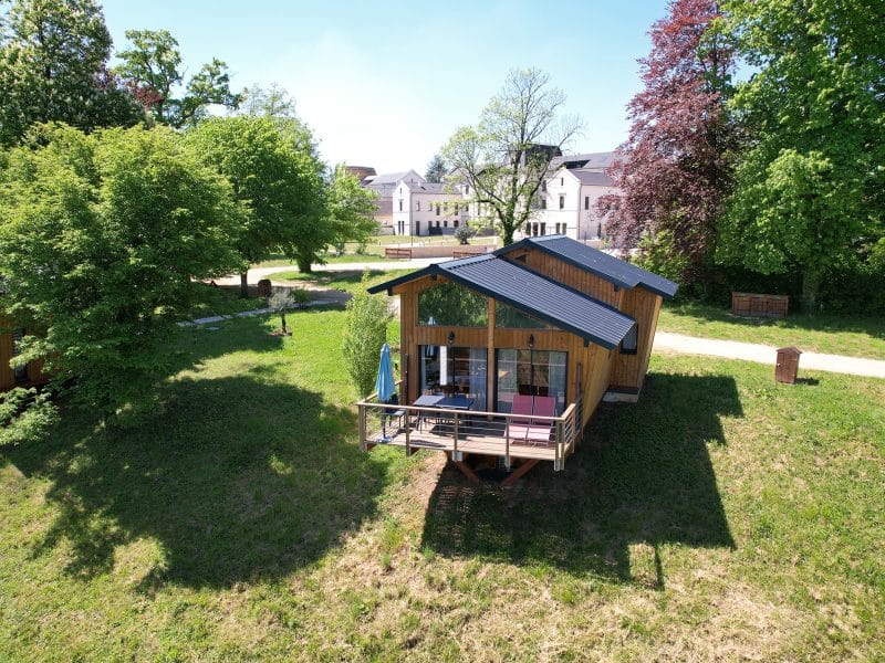 Chalet en bois avec terrasse, entouré de verdure et darbres majestueux.