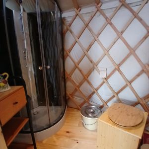 Intérieur d'une yourte avec douche moderne, bois clair et murs en toile. Ambiance cosy et originale.