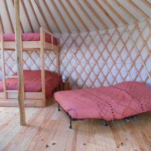 Intérieur d'une yourte avec lits superposés et un lit double, ambiance chaleureuse en bois.