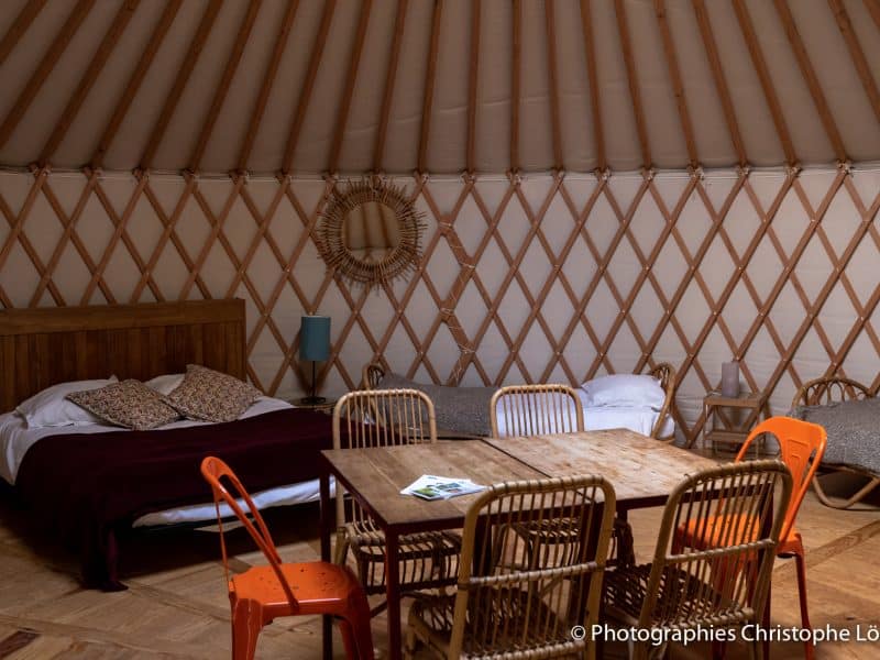 Yourte spacieuse avec lits confortables et table en bois au centre. Ambiance chaleureuse.