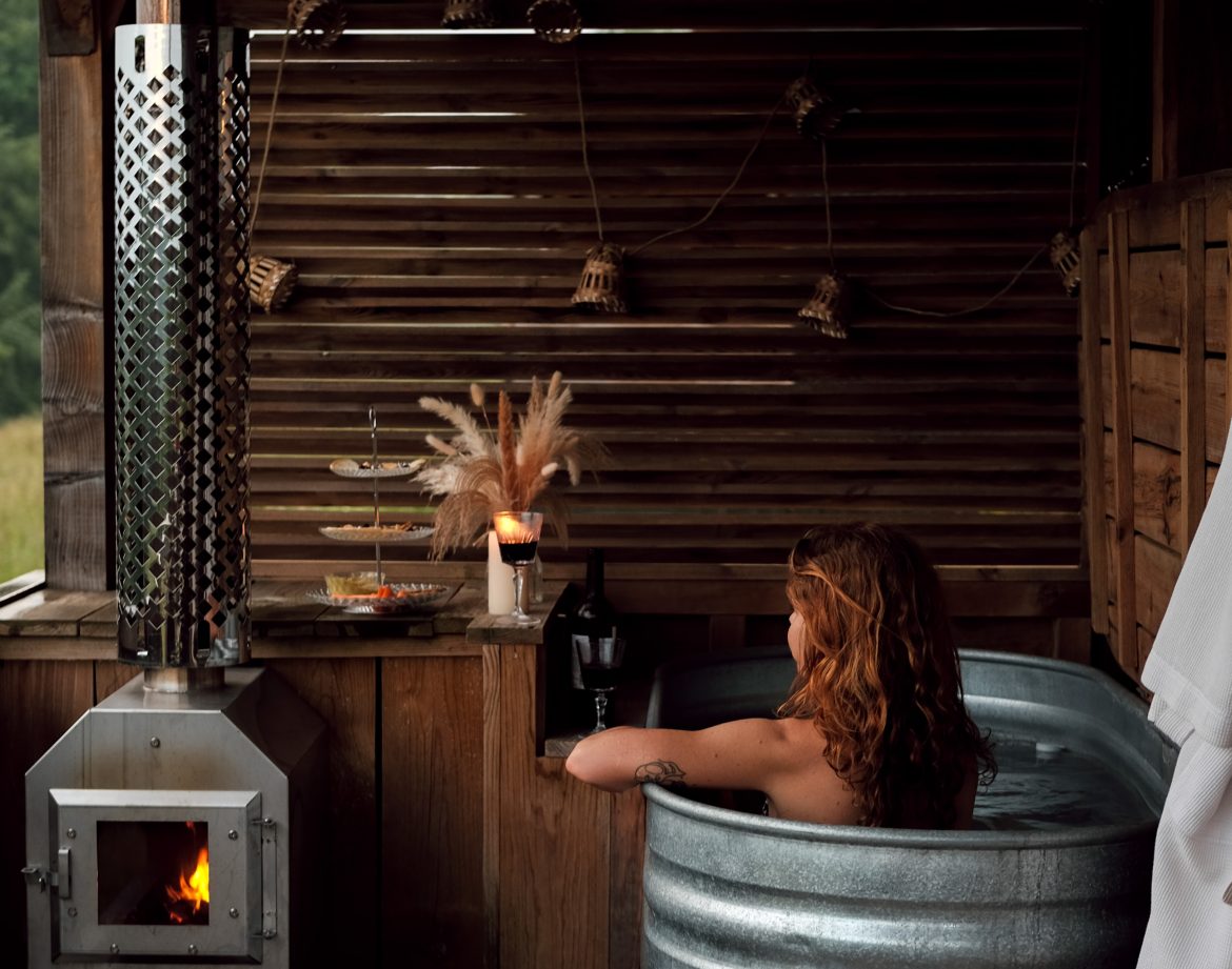 Bain nordique en métal, ambiance chaleureuse avec poêle à bois et décor naturel.