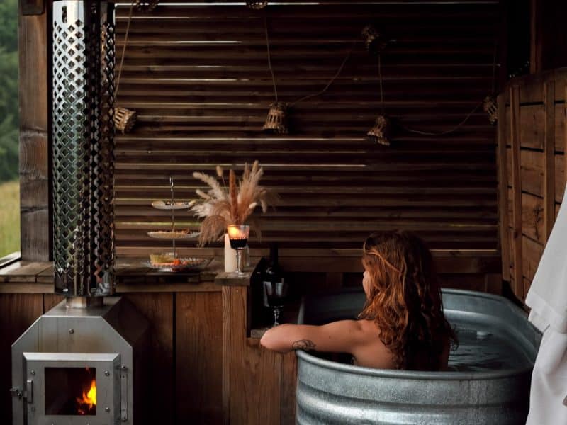Bain nordique en métal, ambiance chaleureuse avec poêle à bois et décor naturel.