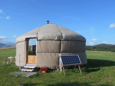 Yourte spacieuse en pleine nature, avec panneaux solaires et vue sur les collines verdoyantes.