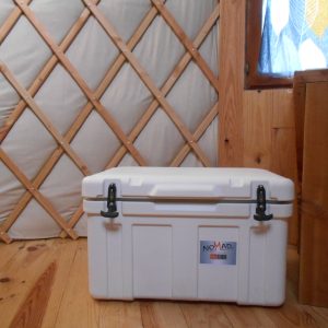 Intérieur d'une yourte avec un coffre de rangement blanc sur un sol en bois.