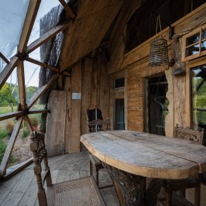 Cabane en bois avec une grande table rustique et des fenêtres panoramiques sur la nature.