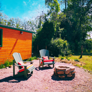 Cabane en bois avec chaises Adirondack et un coin feu, entourée de verdure.