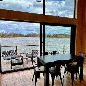 Cabane moderne avec grandes fenêtres, vue sur l'eau et mobilier en bois noir.