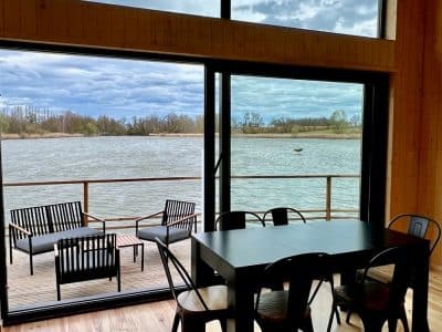 Cabane moderne avec grandes fenêtres, vue sur l'eau et mobilier en bois noir.