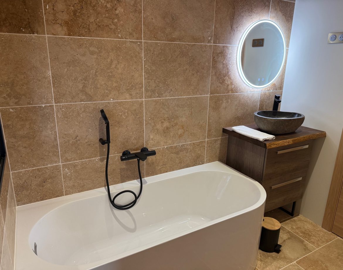 Salle de bain moderne avec baignoire élégante et miroir lumineux, ambiance chaleureuse.