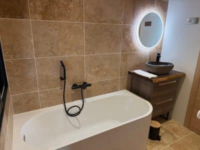 Salle de bain moderne avec baignoire élégante et miroir lumineux, ambiance chaleureuse.