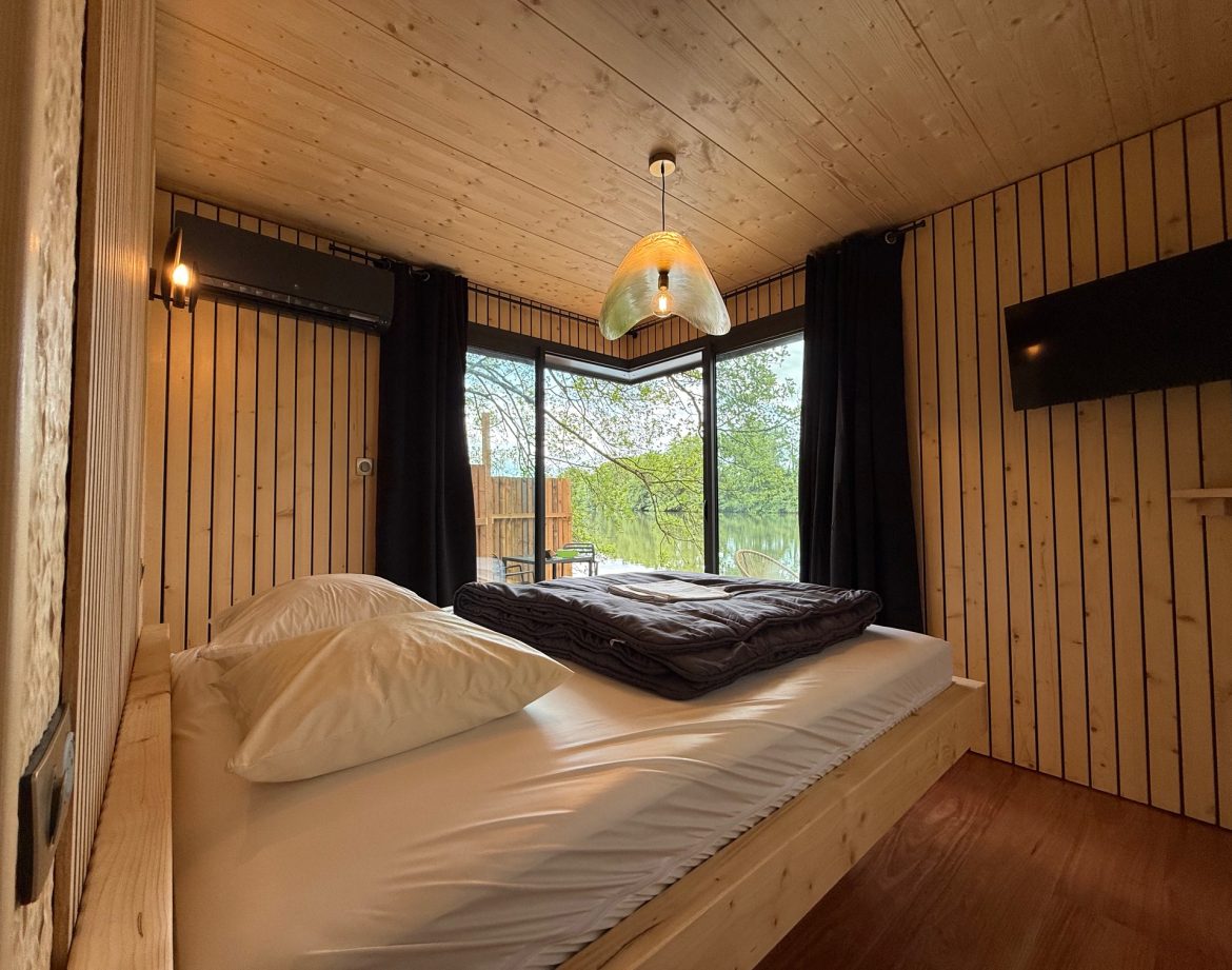 Cabane en bois avec grandes fenêtres, lit douillet et décoration chaleureuse.