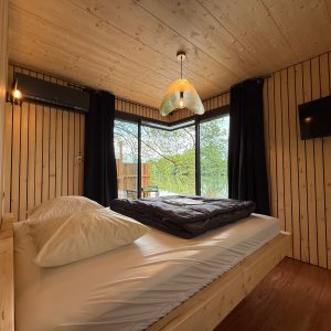 Cabane en bois avec grandes fenêtres, lit douillet et décoration chaleureuse.