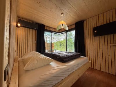 Cabane en bois avec grandes fenêtres, lit douillet et décoration chaleureuse.
