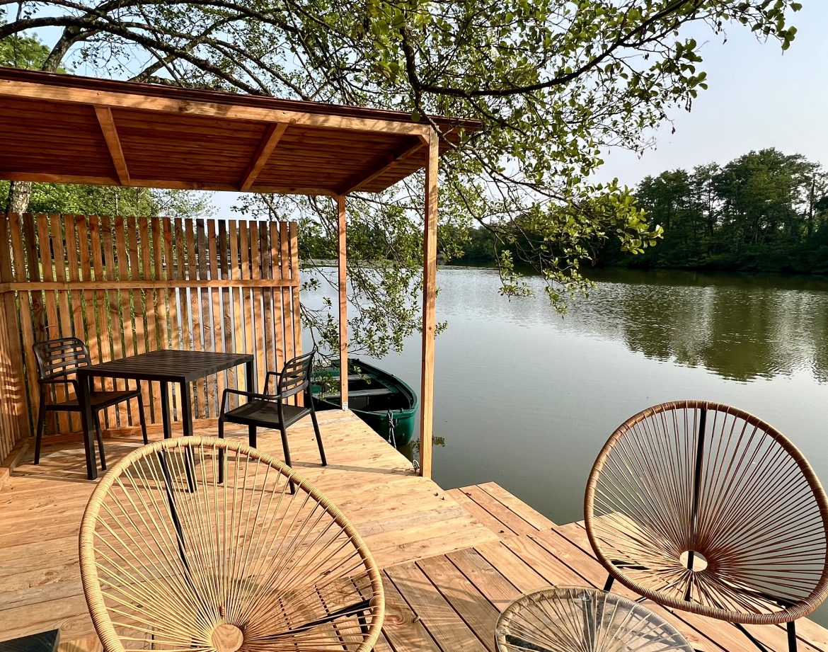 Terrasse en bois surplombant un lac, avec chaises confortables et table pour un séjour paisible.