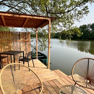 Terrasse en bois surplombant un lac, avec chaises confortables et table pour un séjour paisible.