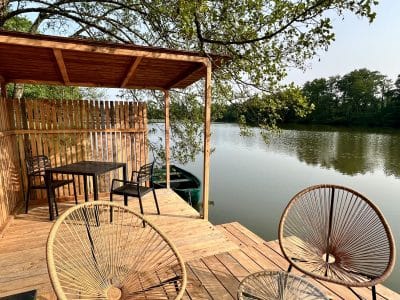 Terrasse en bois surplombant un lac, avec chaises confortables et table pour un séjour paisible.