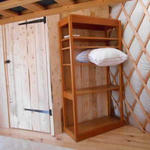Intérieur d'une yourte en bois, avec étagère et lit, ambiance chaleureuse et naturelle.