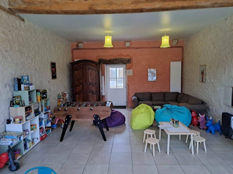 Espace de loisirs dans un gîte, avec jeux, canapés et fauteuils colorés.