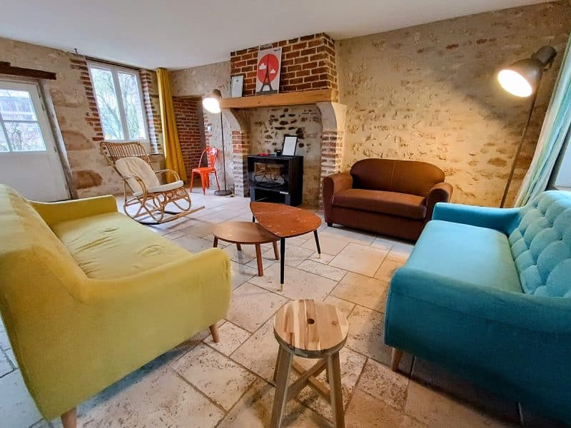 Gîte confortable avec canapés colorés et cheminée en pierre, ambiance chaleureuse.