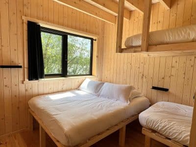 Cabane en bois avec lits superposés, lumière naturelle et vue sur la verdure.