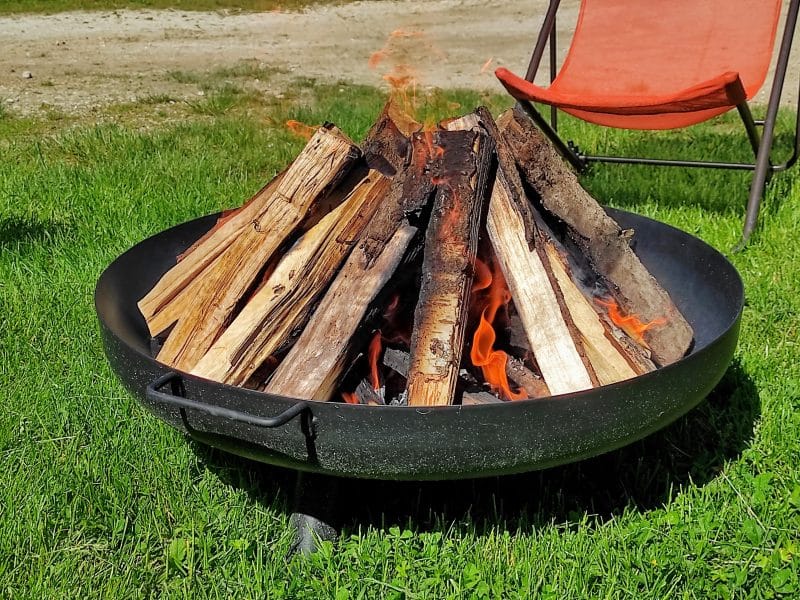 Cheminée extérieure dans un hébergement de camping, entourée de verdure.