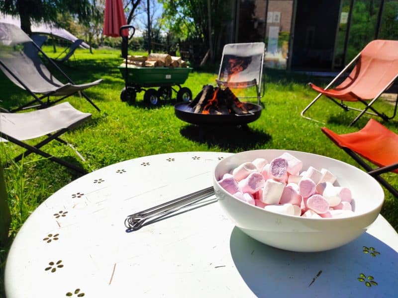 Hébergement en plein air avec feu de camp et chaises confortables dans un jardin verdoyant.