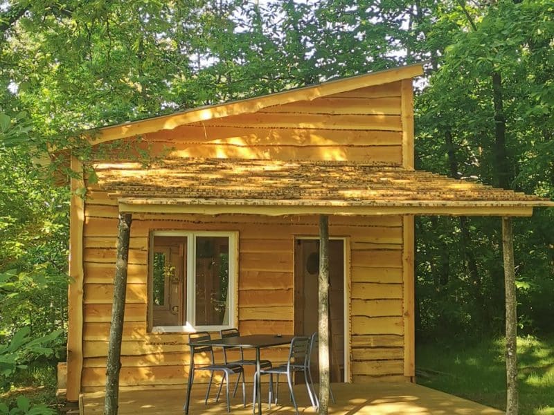 Charmante cabane en bois, entourée d'arbres, avec une terrasse et des chaises.