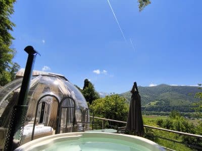 Dôme transparent avec jacuzzi, offrant une vue imprenable sur la montagne et le ciel bleu.