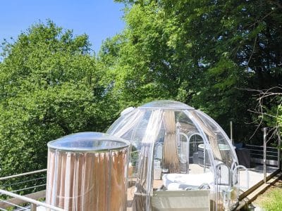 Dôme transparent avec jacuzzi, niché dans la verdure, offrant une vue imprenable sur la nature.