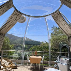 Dôme transparent avec vue panoramique sur la nature, mobilier cosy et lumineux.