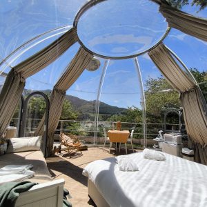 Dôme transparent avec vue panoramique sur la nature, lit confortable et coin repas.