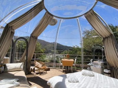 Dôme transparent avec vue panoramique sur la nature, lit confortable et coin repas.