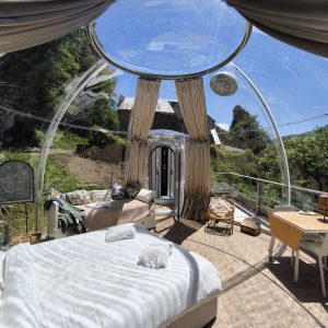 Hébergement insolite : bulle transparente avec vue sur la nature, lit confortable et décor moderne.