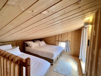 Chalet en bois chaleureux avec deux lits, ambiance cocooning et lumière naturelle.