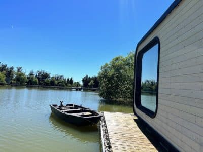 Cabane flottante au bord d'un lac, avec un bateau amarré et un ciel bleu éclatant.