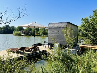 Cabane flottante moderne au bord d'un lac, avec parasol et chaises longues sur la terrasse.