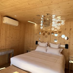 Chalet en bois moderne avec un lit confortable et des miroirs hexagonaux décoratifs.