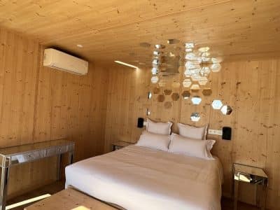 Chalet en bois moderne avec un lit confortable et des miroirs hexagonaux décoratifs.