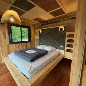 Chambre en bois moderne avec lit king-size, éclairage chaleureux et salle de bain intégrée.