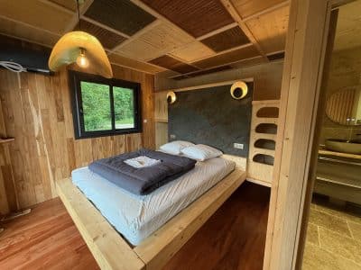 Chambre en bois moderne avec lit king-size, éclairage chaleureux et salle de bain intégrée.