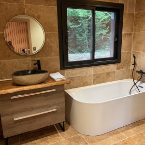 Salle de bain moderne dans un hébergement insolite, avec baignoire élégante et décor en pierre.