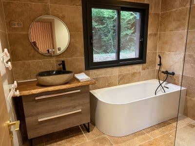 Salle de bain moderne dans un hébergement insolite, avec baignoire élégante et décor en pierre.