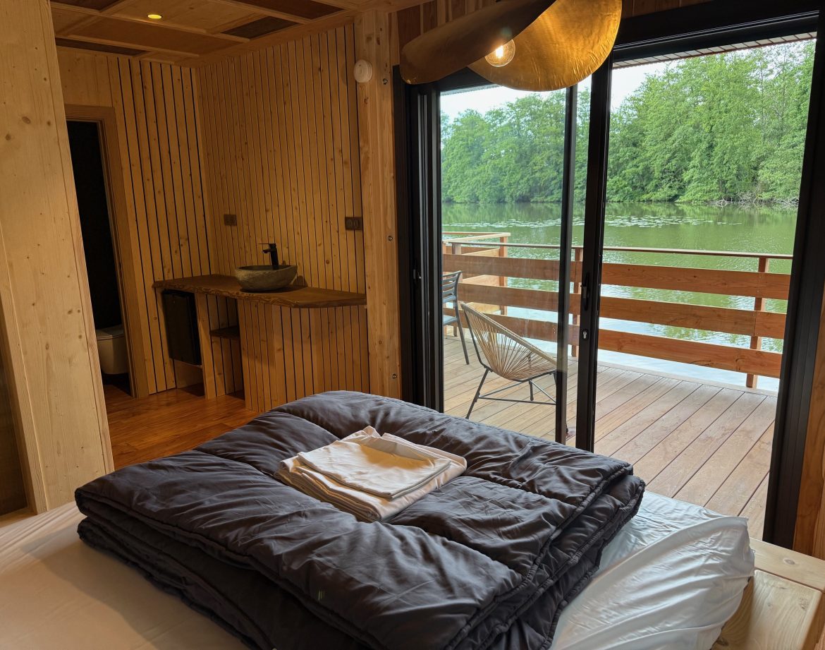 Cabane en bois avec vue sur l'eau, lit confortable et terrasse ensoleillée.
