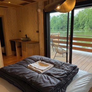 Cabane en bois avec vue sur l'eau, lit confortable et terrasse ensoleillée.
