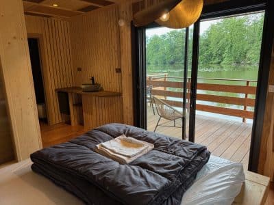 Cabane en bois avec vue sur l'eau, lit confortable et terrasse ensoleillée.